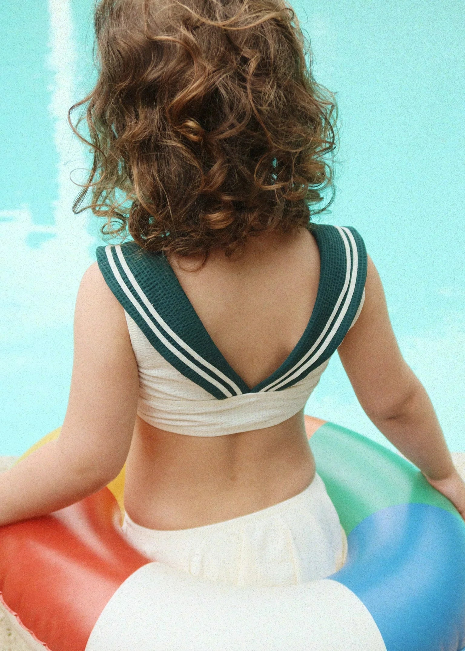 Person wearing a vintage-style sailor top sitting on a colorful inflatable ring by a pool.