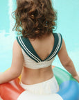 Person wearing a vintage-style sailor top sitting on a colorful inflatable ring by a pool.