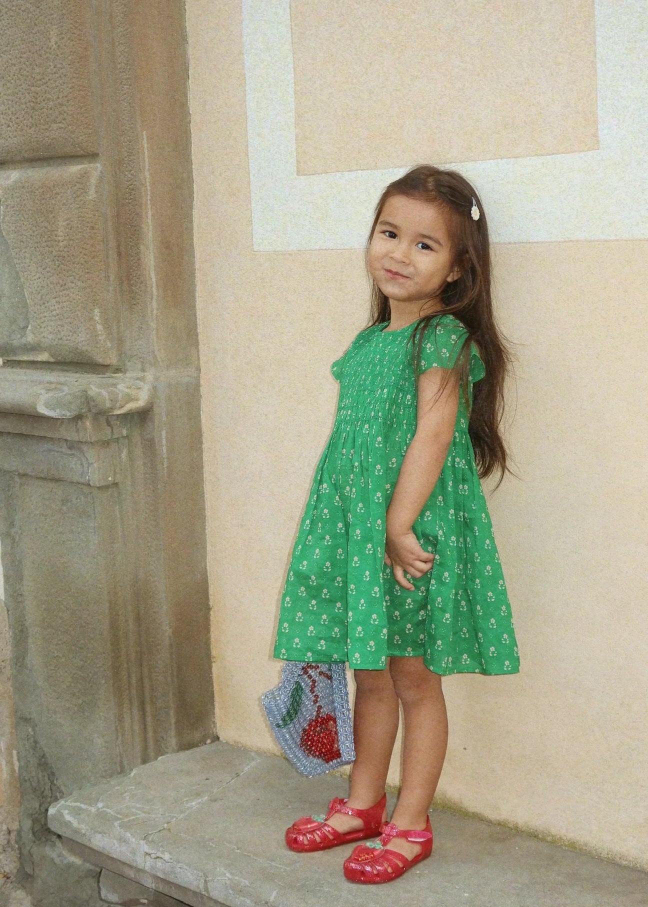 Young girl in a green dress standing on stone steps with a decorative wall behind her