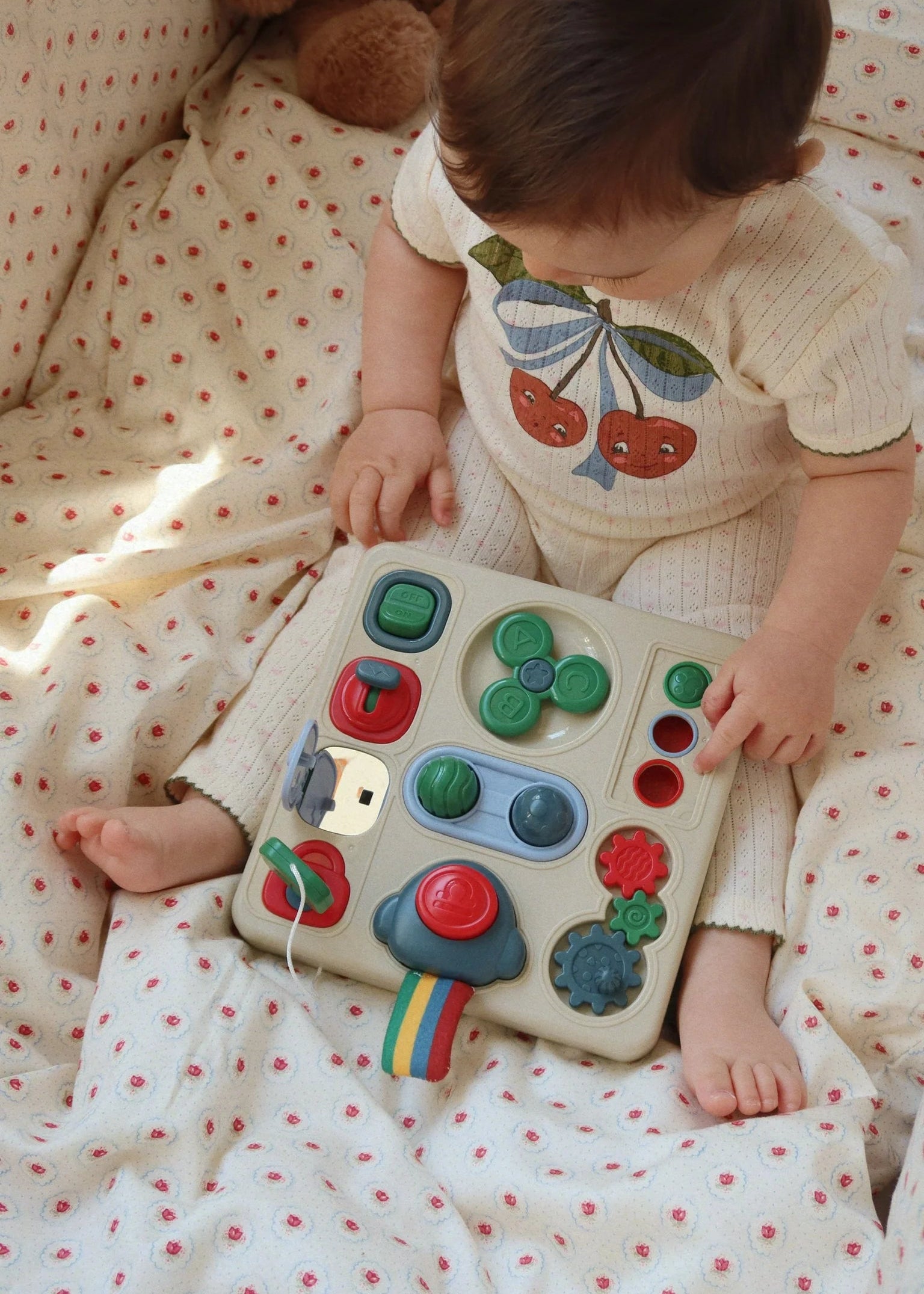 Baby playing with a colorful toy on a polka dot blanket