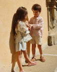 Two children standing close to each other in front of a beige wall.