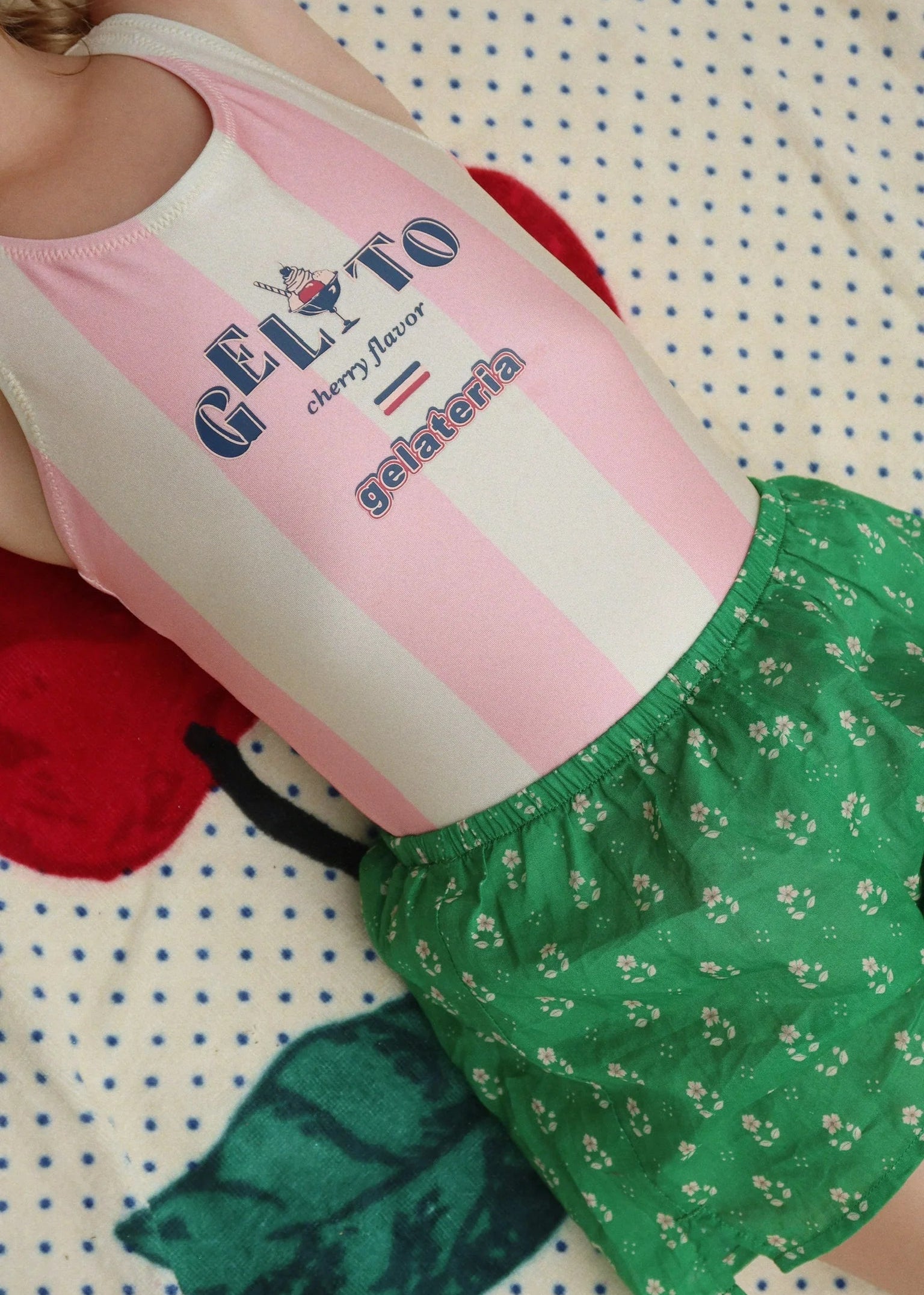 Person wearing a pink and white sleeveless top with 'Gelato' text and green shorts on a polka dot background.