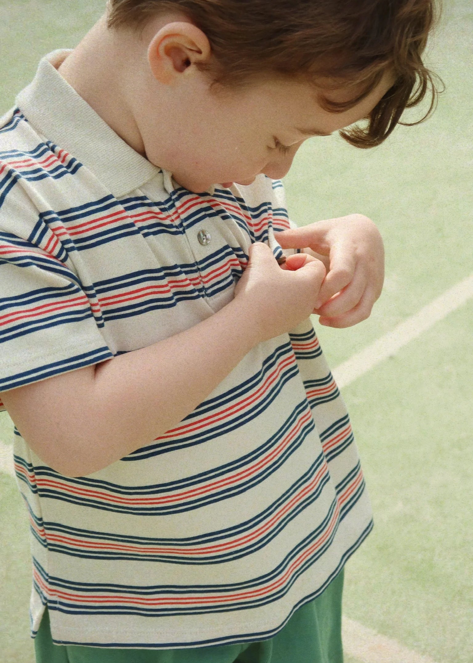Child wearing a striped polo shirt on a light green background