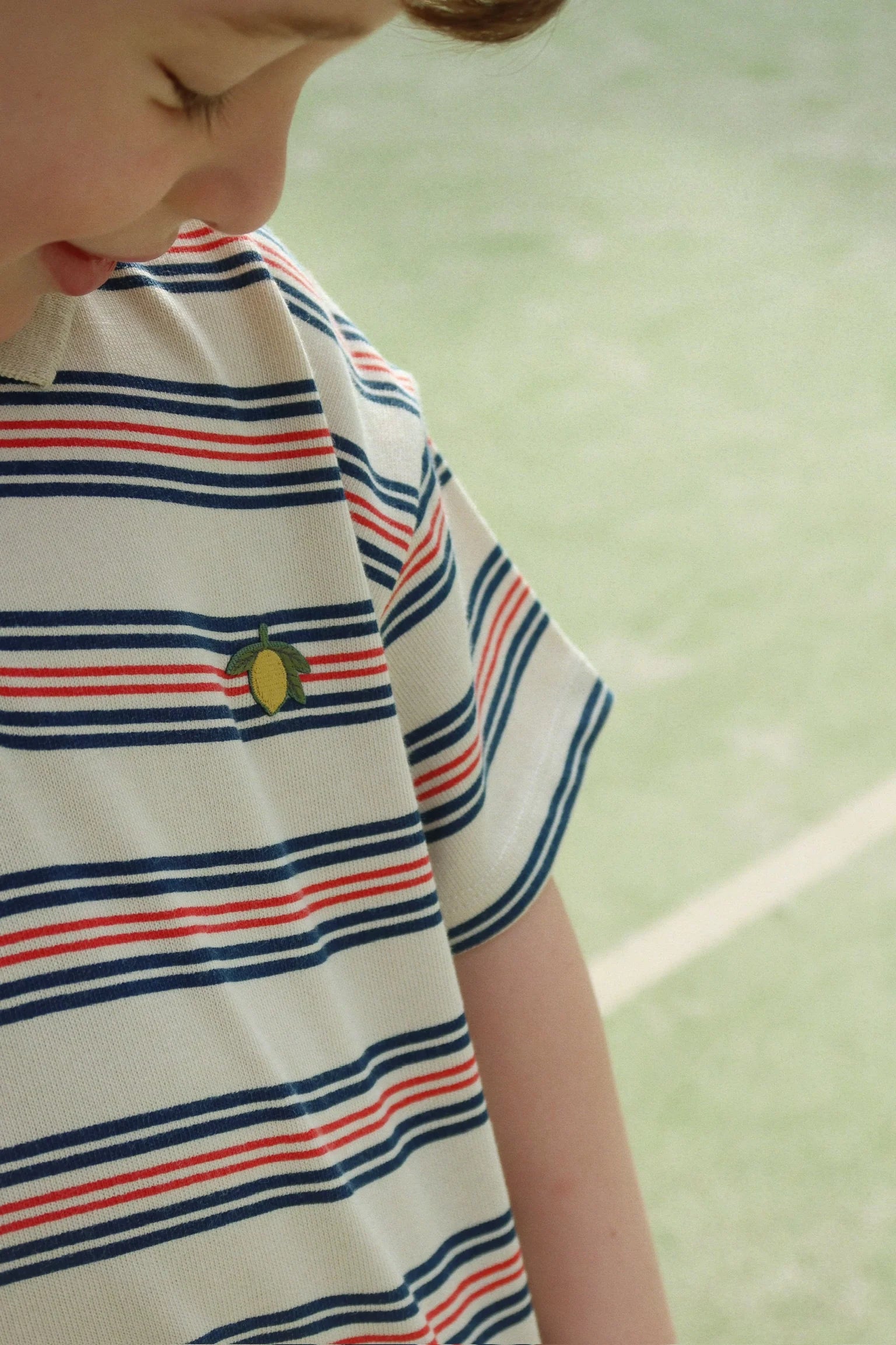 Child wearing a striped shirt with a small logo on a green background