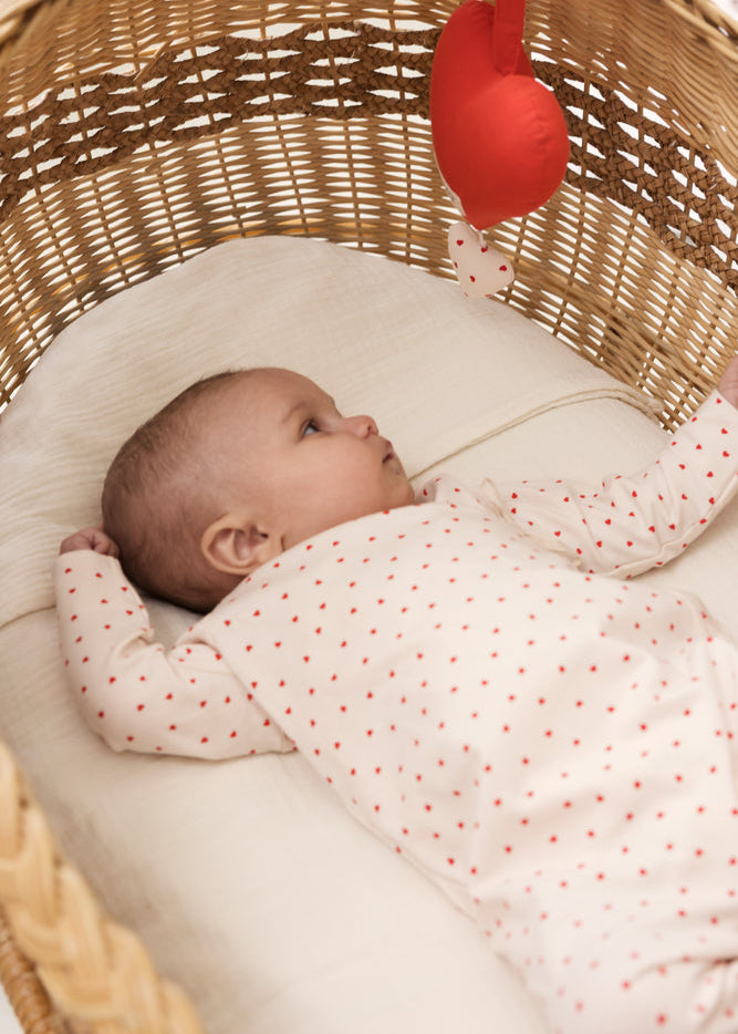 Baby lying in a wicker crib with a red hanging toy
