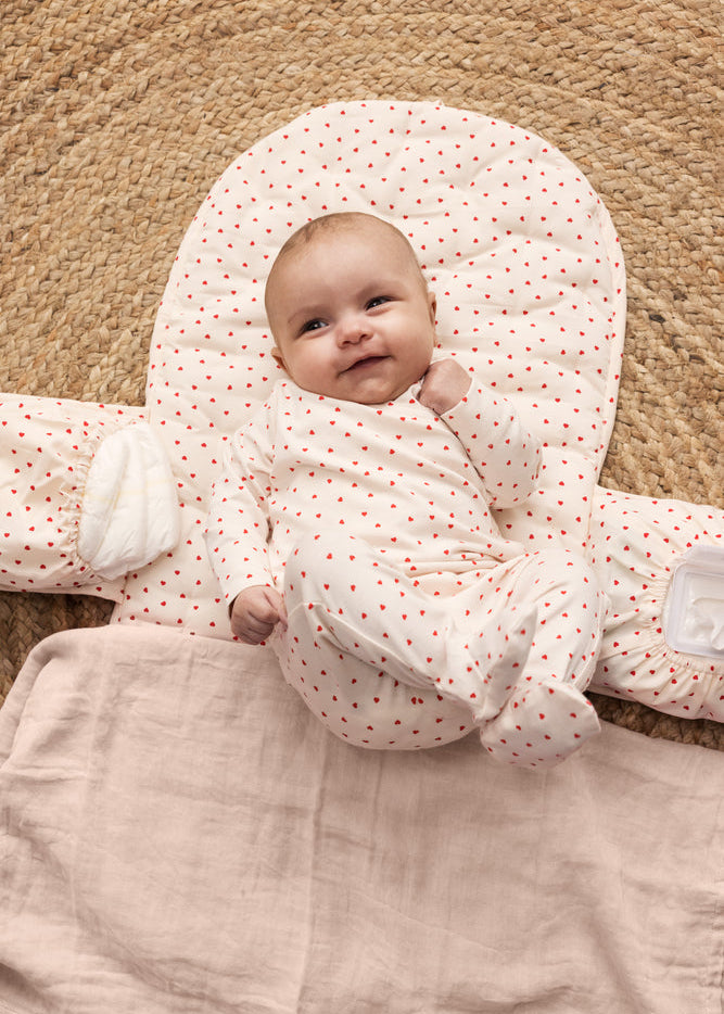 Baby wrapped in a pink blanket with white polka dots on a beige carpet