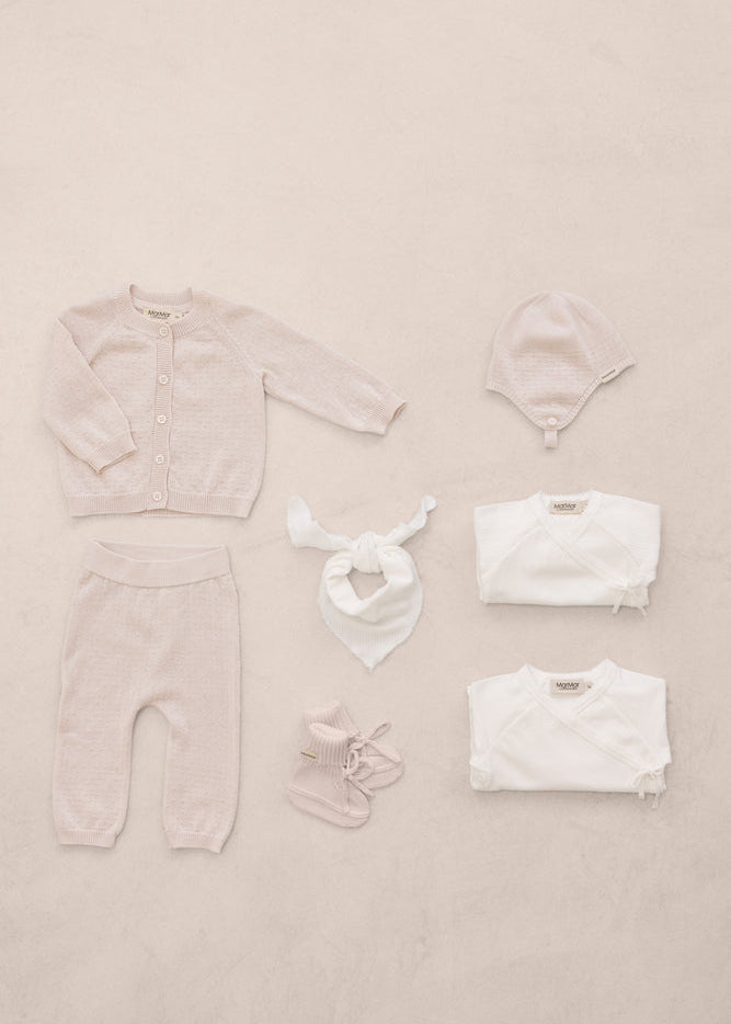 Baby clothing set including a onesie, hat, and booties on a beige background