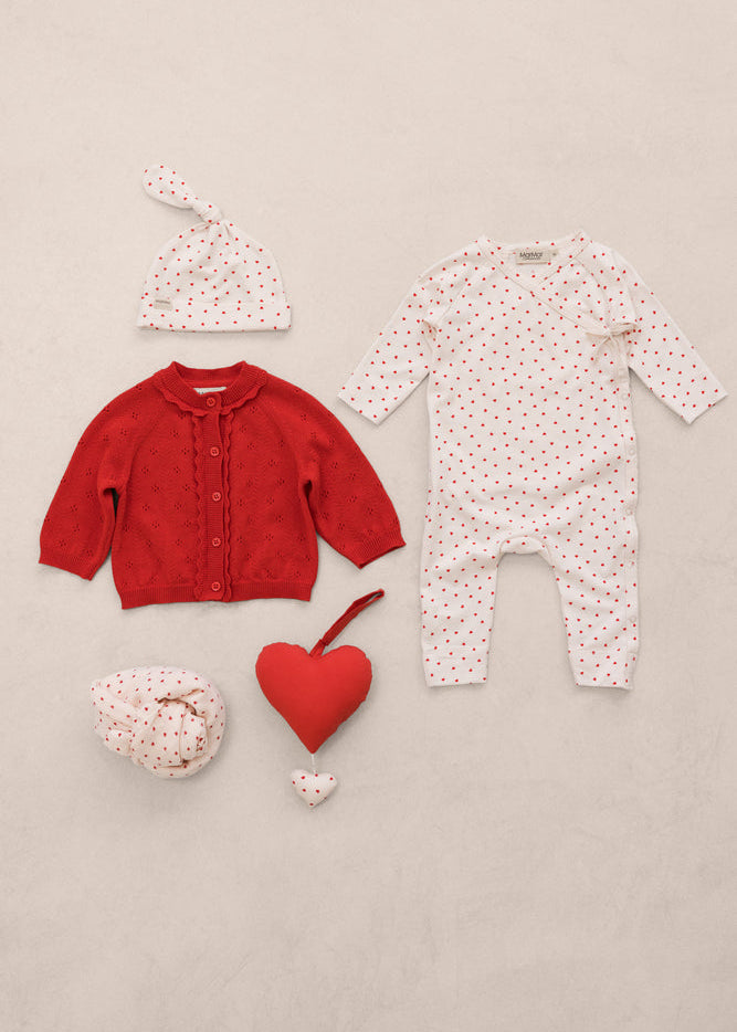 Baby clothing set with red cardigan, white onesie, and matching hat on a beige background