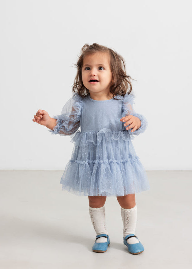Child wearing a blue dress with long sleeves on a white background