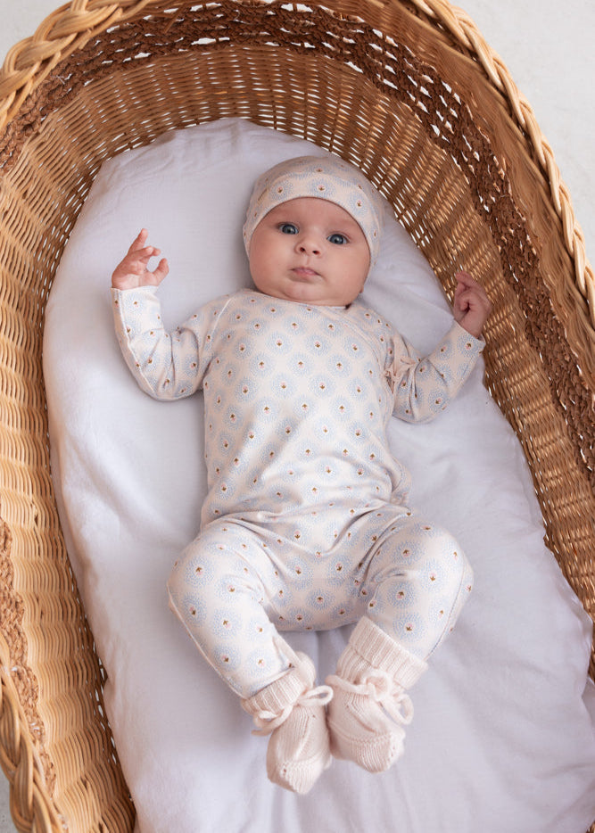 Baby in a white outfit with polka dots lying in a wicker crib.