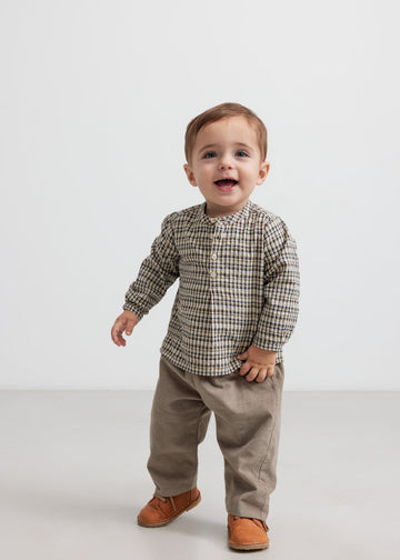 Child wearing a plaid shirt and beige pants on a white background