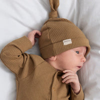 Baby wearing a brown knit outfit and hat on a white bed