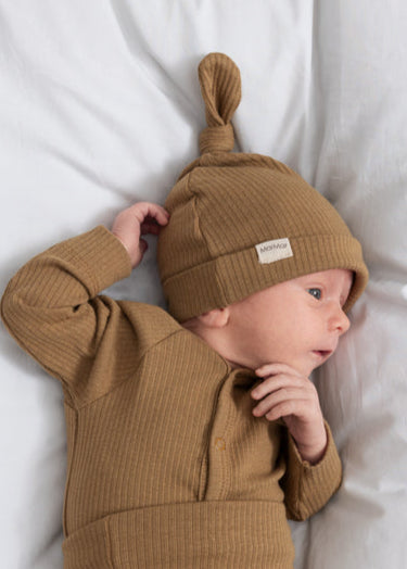 Baby wearing a brown knit outfit and hat on a white bed