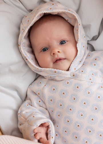 Baby wearing a floral patterned outfit lying on a soft surface