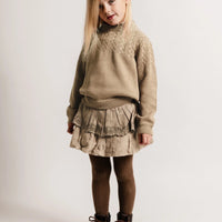 Young girl wearing a beige sweater and skirt with brown boots on a white background