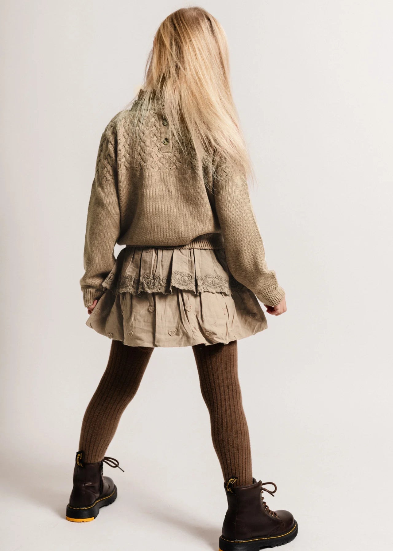 Person wearing a beige jacket and skirt with brown tights and black shoes on a white background
