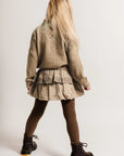 Person wearing a beige jacket and skirt with brown tights and black shoes on a white background