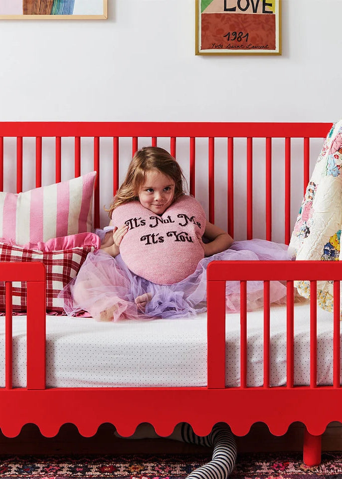 Child in a red crib with a pink pillow and colorful bedding