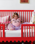 Child in a red crib with a pink pillow and colorful bedding