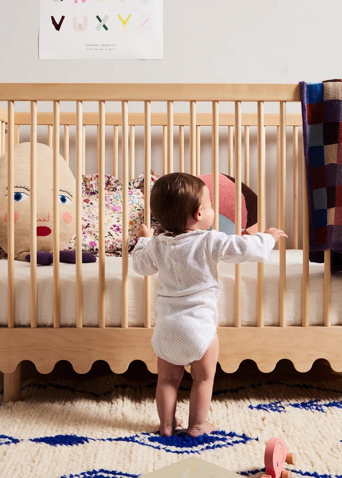 Baby standing next to a crib with colorful toys and a blanket