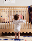 Baby standing next to a crib with colorful toys and a blanket
