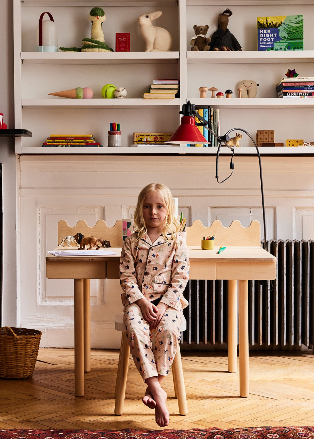 Child sitting at a small wooden table in a room with shelves filled with various items.