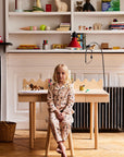 Child sitting at a small wooden table in a room with shelves filled with various items.