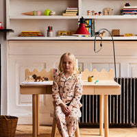 Child sitting at a small wooden table in a room with shelves filled with various items.