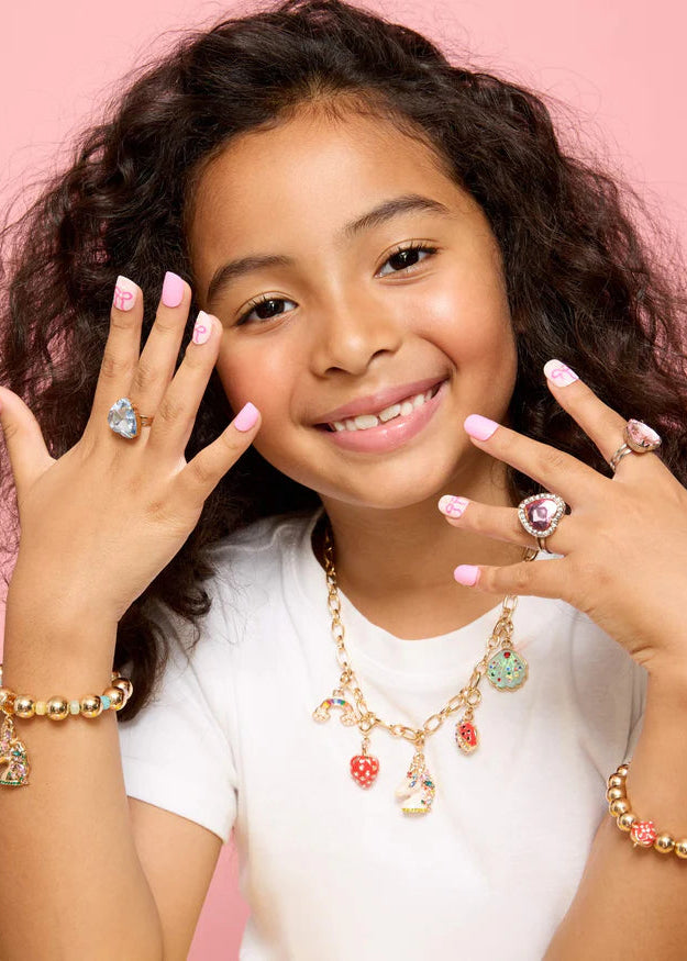 Young girl wearing multiple pieces of jewelry including rings and a necklace on a pink background