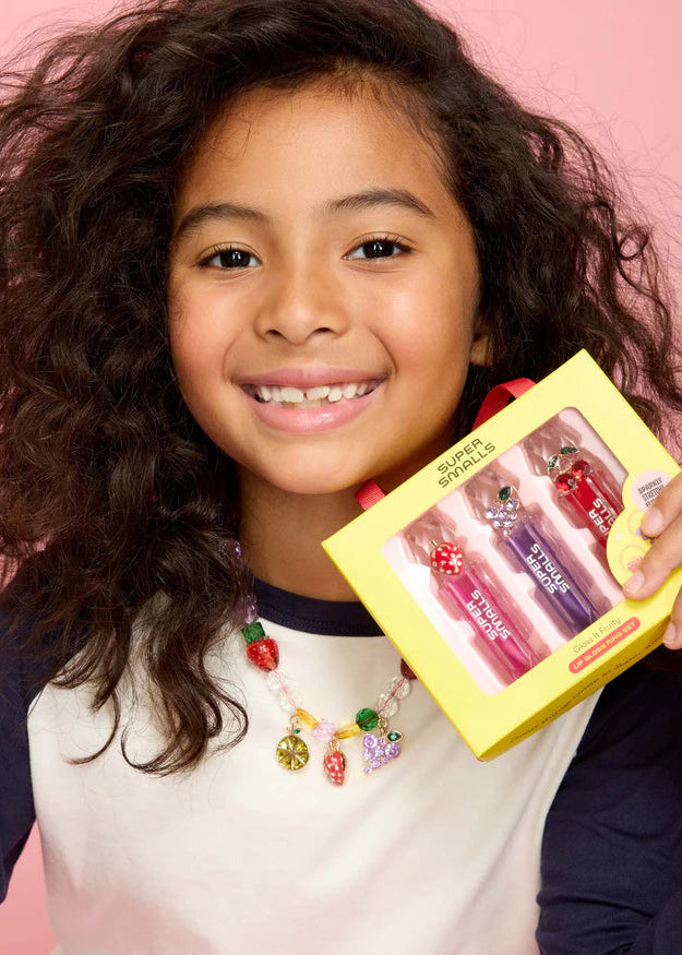 Young girl holding a yellow box with lip balms against a pink background