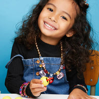 Young girl with colorful jewelry holding a small object against a blue background