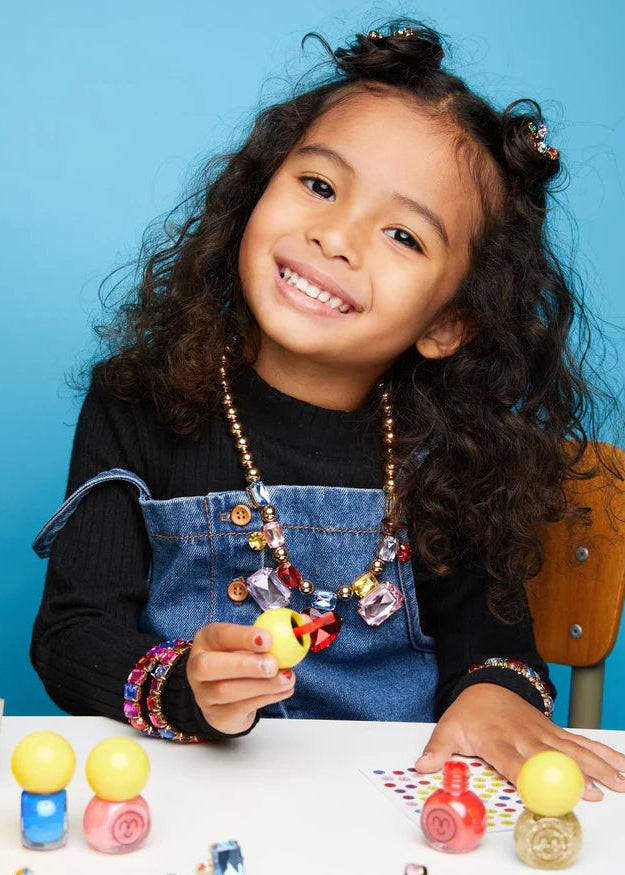 Young girl with colorful jewelry holding a small object against a blue background