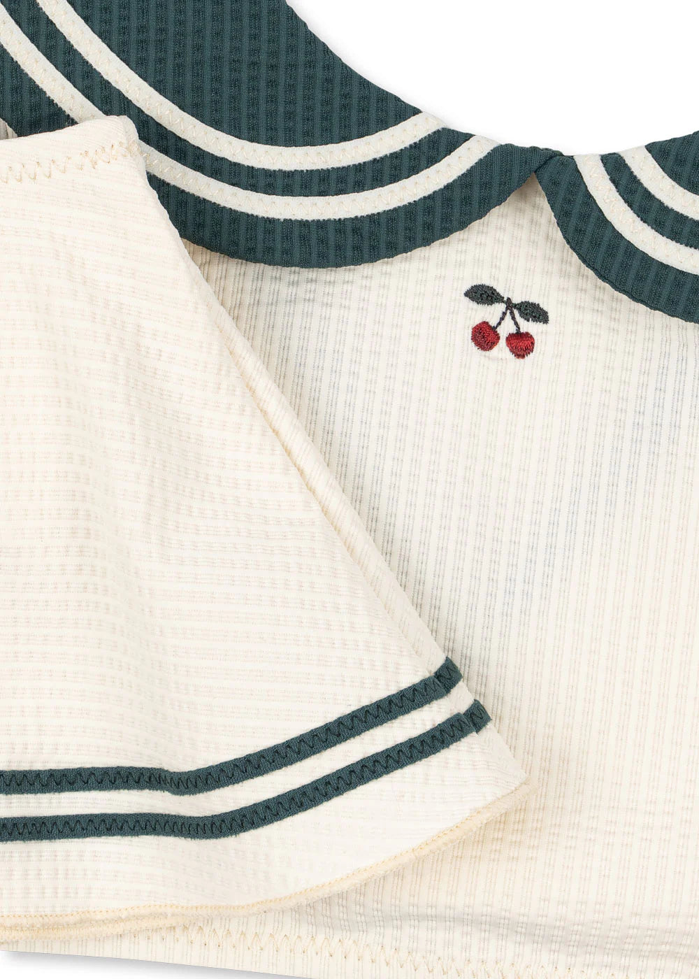 Close-up of a baby outfit with green trim and cherry design on a white background