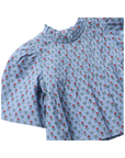 A close-up of a light blue short-sleeve blouse with a pleated texture and an all-over small floral print featuring red roses and white blossoms with green leaves.