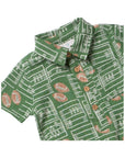 A close-up of a green short-sleeve collared shirt with a white football field line pattern and brown football motifs, featuring three brown buttons on the front.
