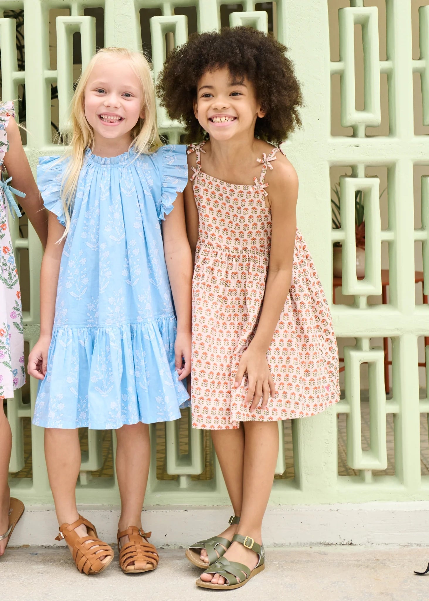 Two young girls wearing dresses standing in front of a decorative wall.