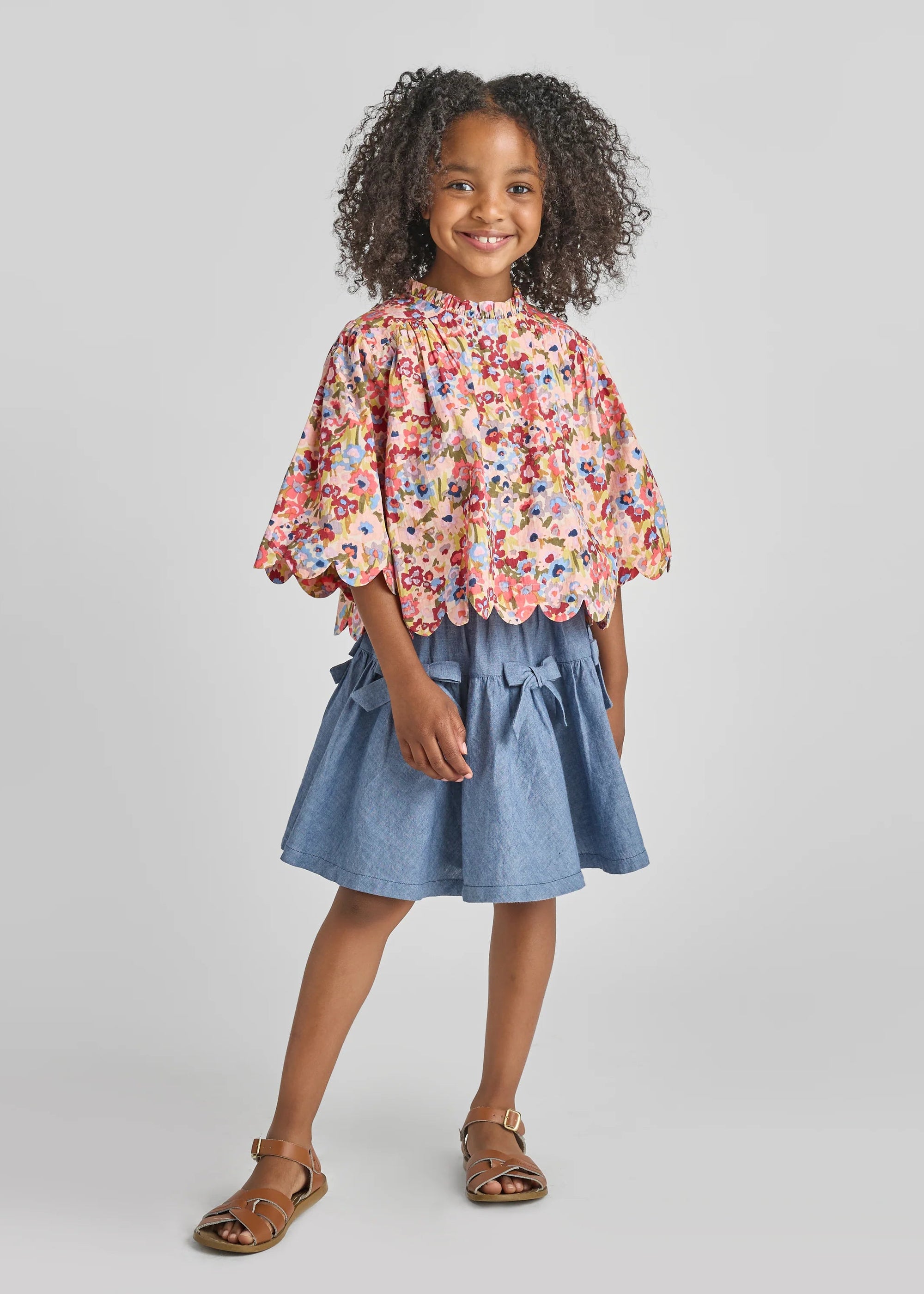Young girl wearing a floral blouse and denim skirt on a gray background