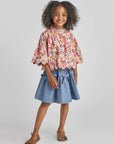 Young girl wearing a floral blouse and denim skirt on a gray background