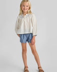Young girl wearing a white blouse and blue shorts on a gray background