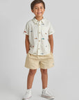 Child wearing a white shirt with colorful buttons and beige shorts on a light gray background