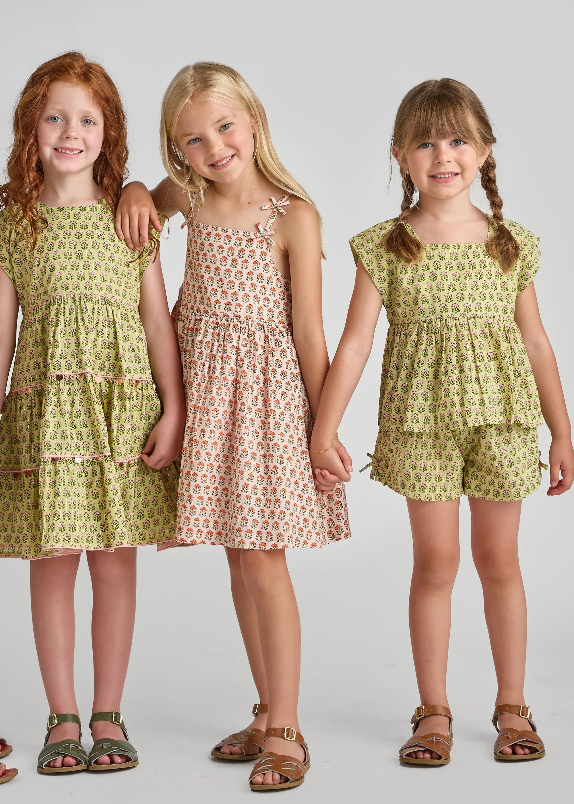 Three young girls wearing matching green dresses with floral patterns on a plain background