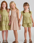 Three young girls wearing matching green dresses with floral patterns on a plain background