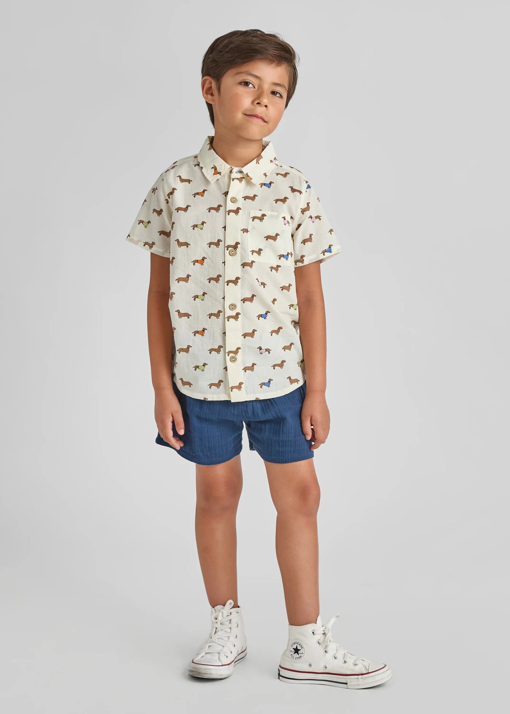 Child wearing a patterned shirt and denim shorts on a plain background
