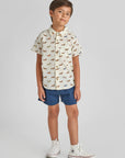 Child wearing a patterned shirt and denim shorts on a plain background