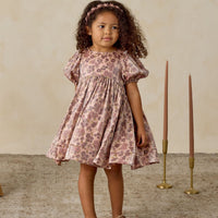 Young girl in a floral dress standing in a room with candles and a vase.