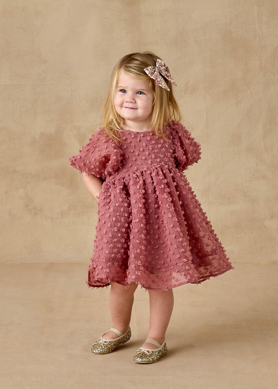 Young girl in a pink dress with a floral headband against a beige background