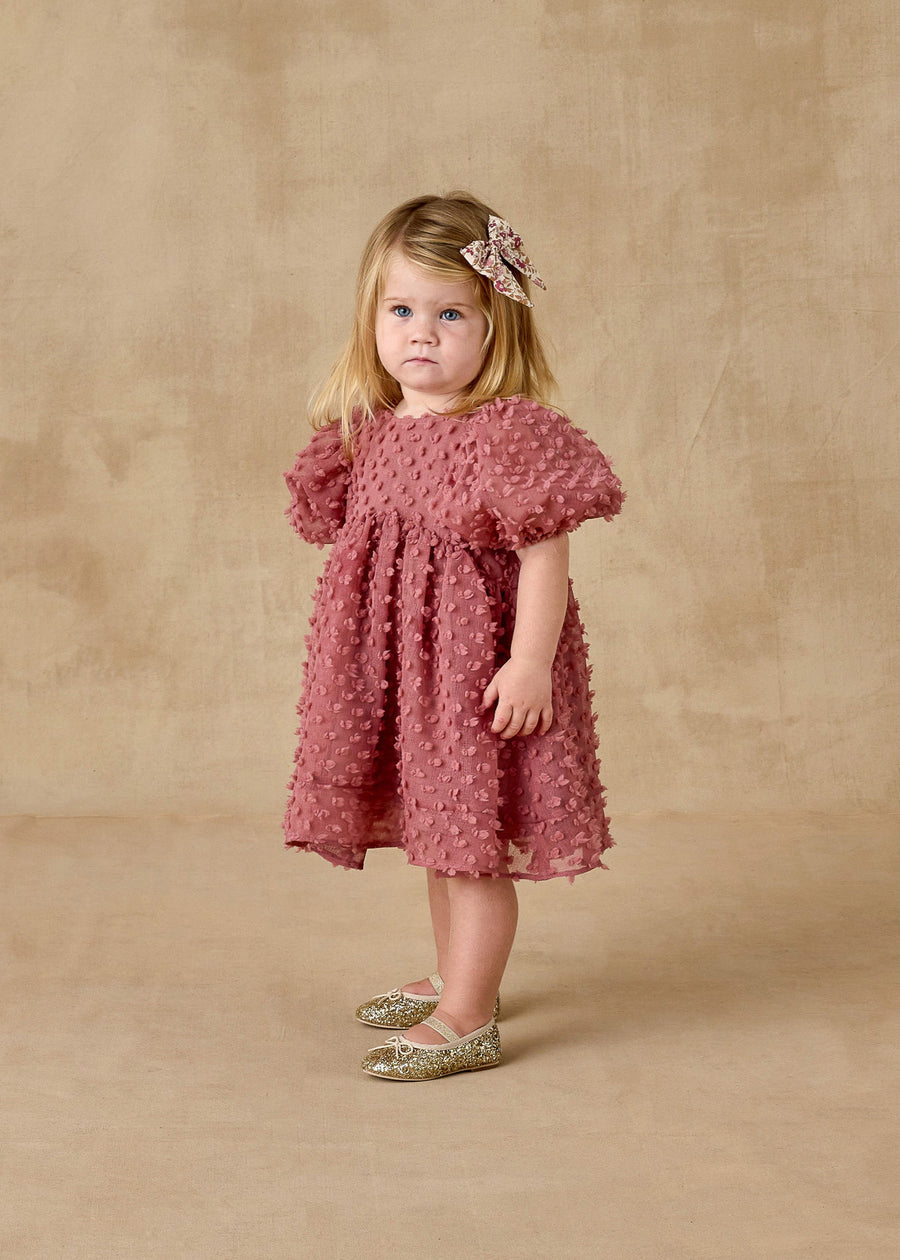 Young girl wearing a pink dress with ruffled sleeves against a beige background