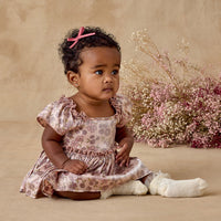 Baby girl in a floral dress sitting on a beige background with pink flowers.