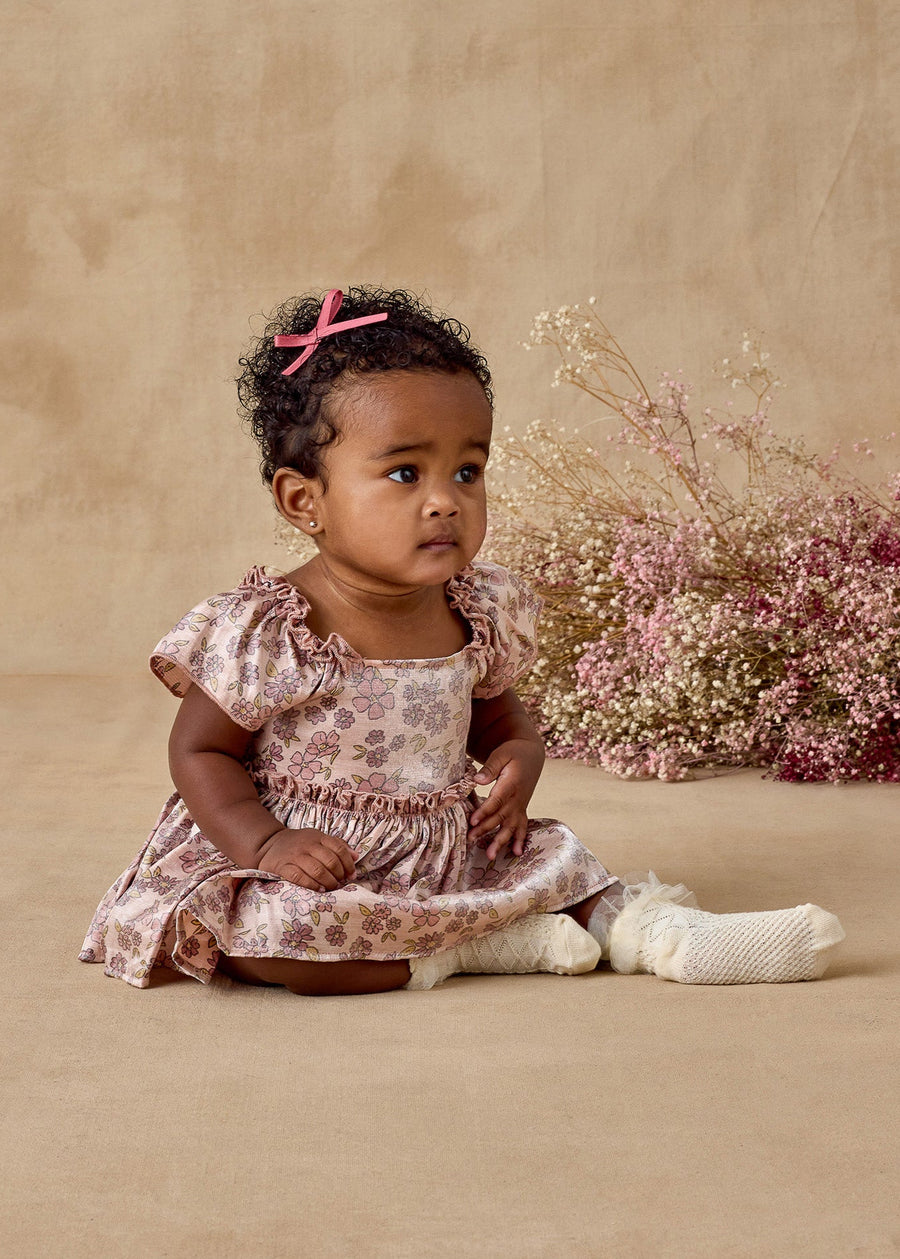 Baby girl in a floral dress sitting on a beige background with pink flowers.