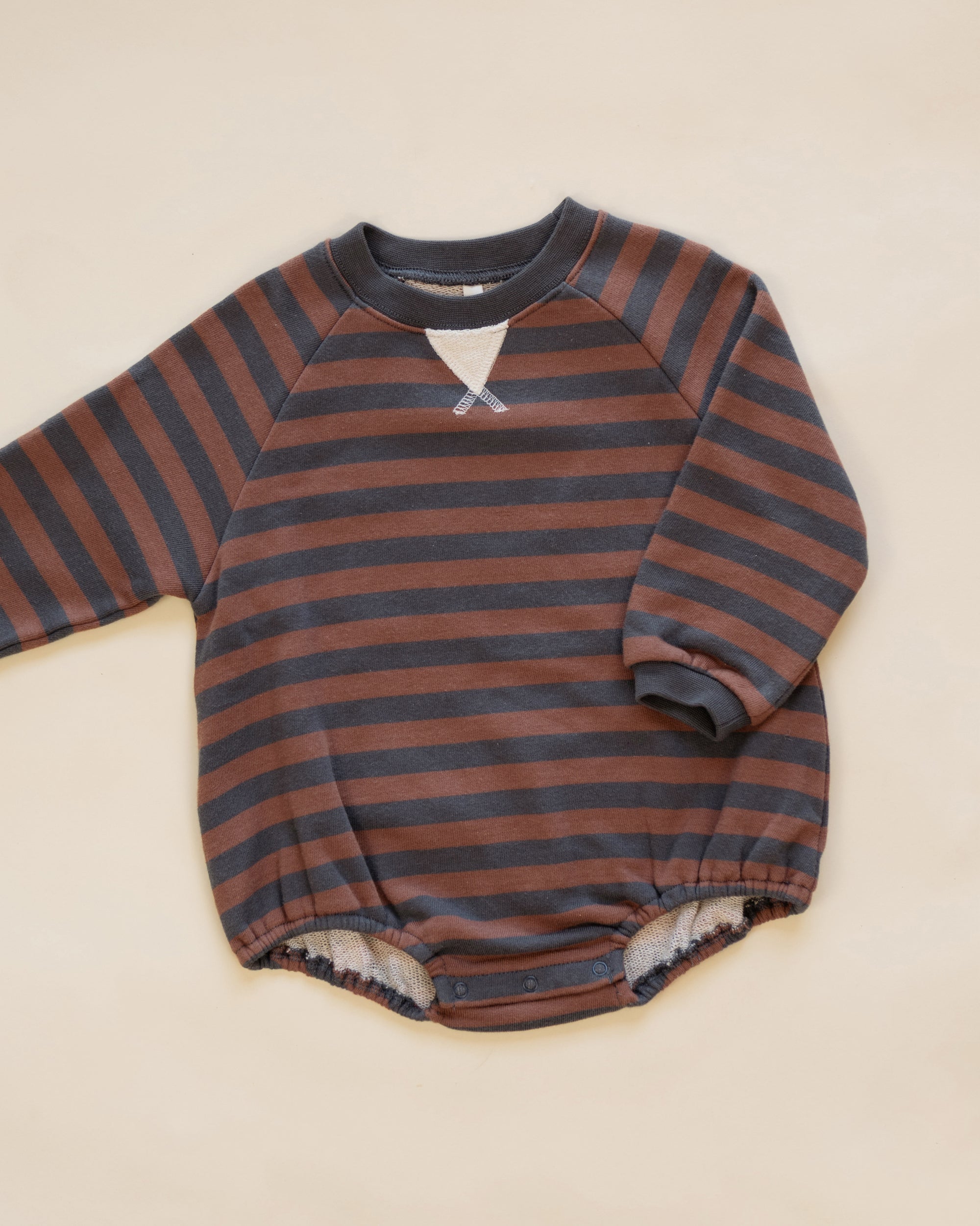 A baby long-sleeve romper with horizontal rust brown and dark gray stripes, featuring a small white V-shaped detail at the neckline and a soft fleece lining at the leg openings, laid flat on a light beige background.
